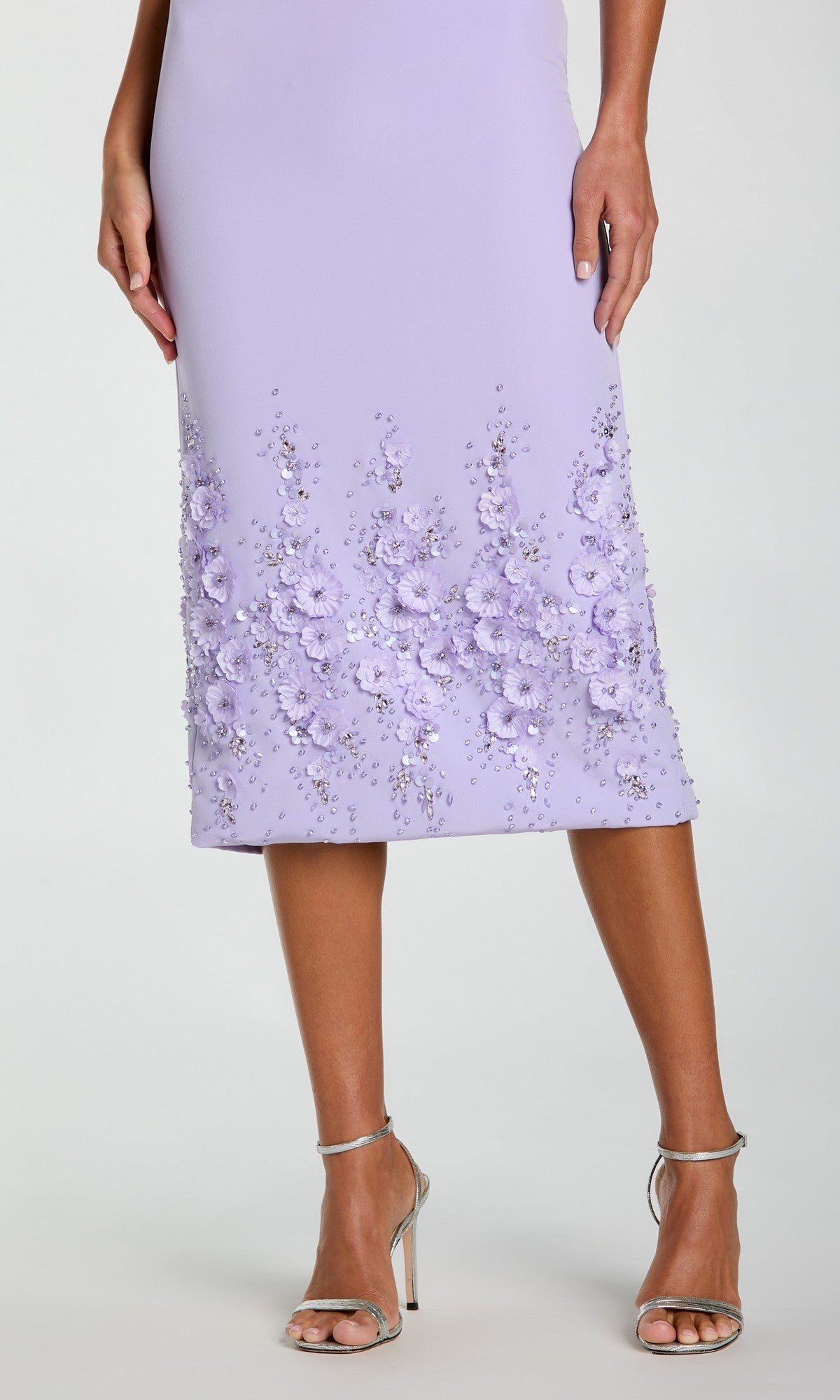 A woman wearing the Mac Duggal 11853 Midi Sheath Wedding Guest Dress—sleeveless, light purple, with beaded 3-D flowers and sequined hem—paired with silver high-heeled sandals.