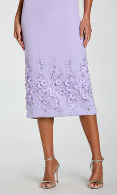 A woman wearing the Mac Duggal 11853 Midi Sheath Wedding Guest Dress—sleeveless, light purple, with beaded 3-D flowers and sequined hem—paired with silver high-heeled sandals.