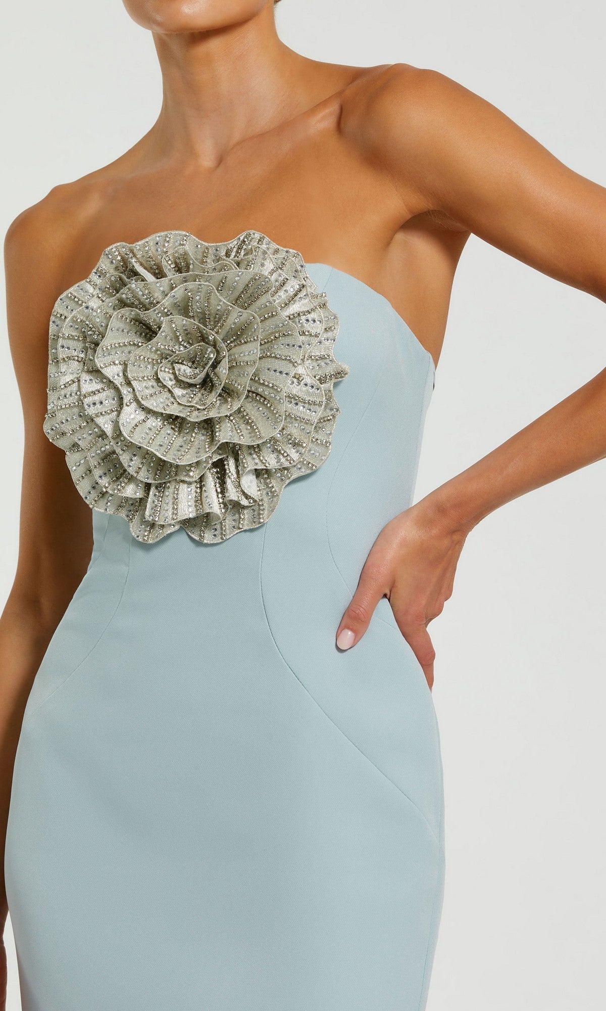 A woman wears the Mac Duggal 11855 Strapless Floral Formal Gown in light blue, featuring a large silver ruffled flower on the bodice—an elegant pick for evening events.