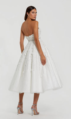 Woman wearing the Mac Duggal 11865 Strapless Champagne Party Dress with embellishments and silver heels, standing on a light background and glancing over her shoulder.
