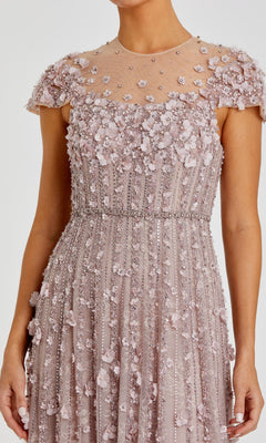 A woman wears the Mac Duggal 11866 Long Beaded Lilac Formal Dress, featuring 3-D floral appliques and intricate beadwork on a sheer bodice and skirt.