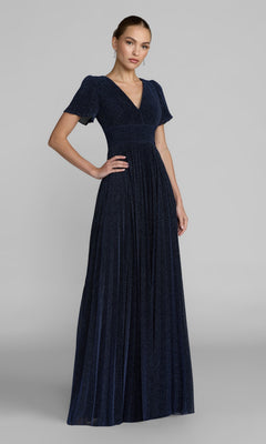 A woman in a floor-length, dark blue Mac Duggal 11881 Short Sleeve Pleated Formal Gown with a V-neckline stands against a plain gray background.