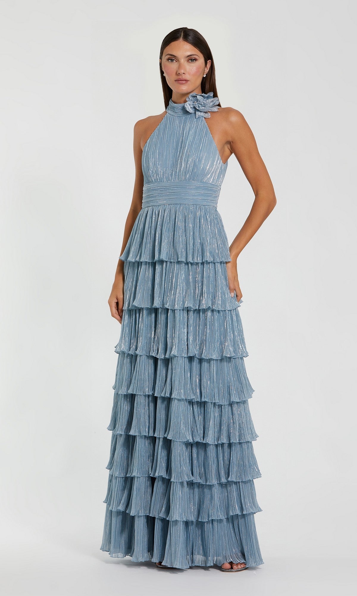 A woman stands against a plain light background wearing the Mac Duggal 11882 long formal dress in powder blue, featuring a sleeveless halter-neck design, tiered ruffle skirt, and floral detail at the neckline.