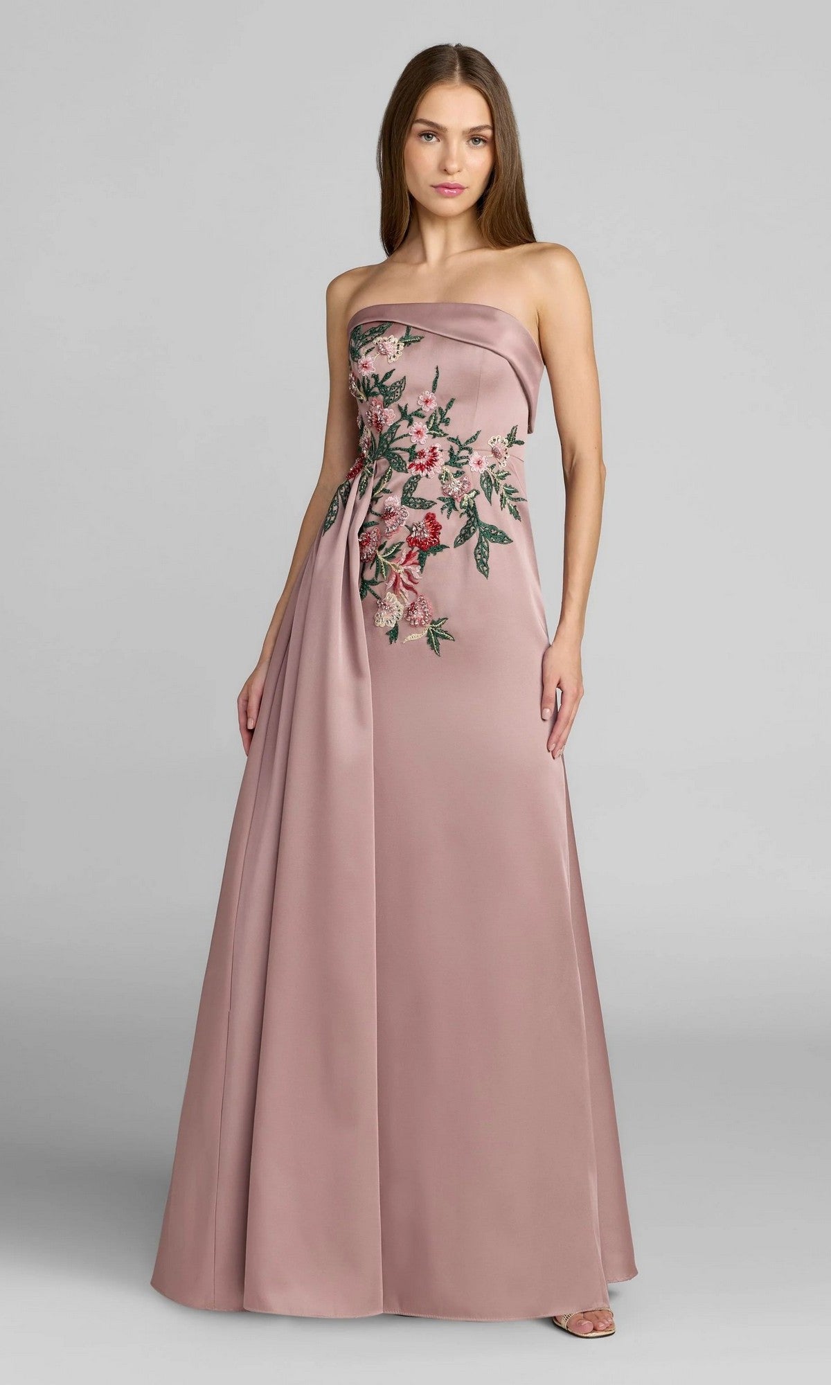 Wearing the Mac Duggal 11894 Long Formal Dress—a strapless, floor-length A-line gown in dusty rose satin with floral embroidery on the bodice—a woman stands against a plain gray background.