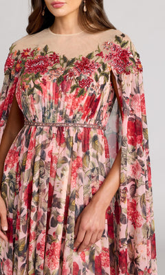A woman wears the Mac Duggal 11907 long formal dress, featuring a sheer design with embroidered red and pink flowers, green leaves, and flowing cape sleeves. Only the upper half of her body is visible.
