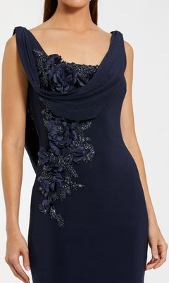A woman wearing the Mac Duggal 11910 sleeveless navy blue cowl-neck long formal dress, featuring elegant floral appliqué on the bodice, captures timeless evening style.