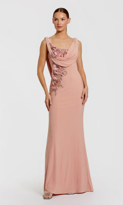 A woman stands against a plain white background wearing the Mac Duggal 11910 cowl-neck long formal dress—a sleeveless blush pink gown featuring draped detailing and floral embellishments on the bodice.