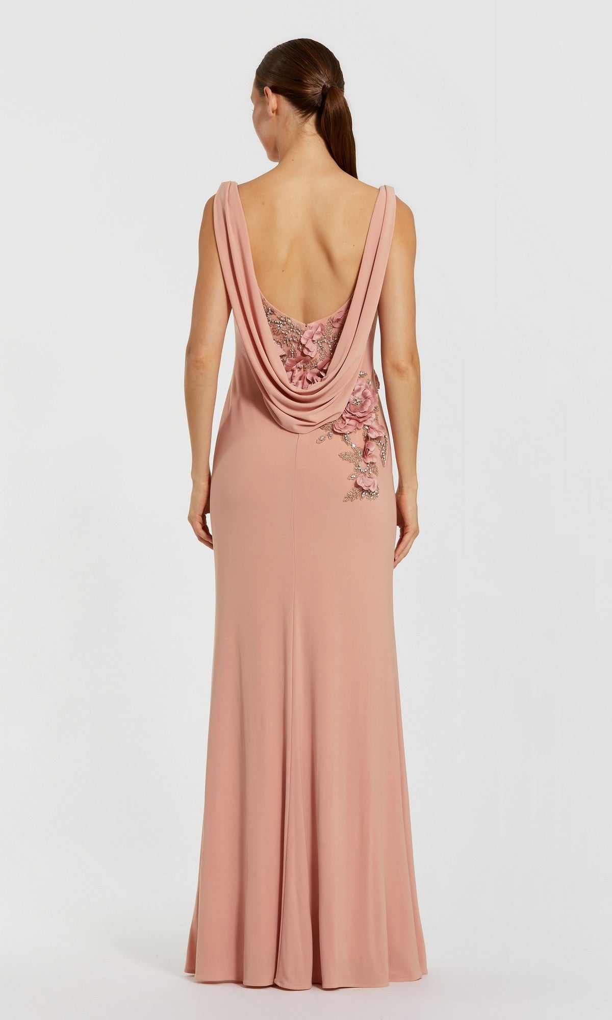 A woman stands facing away against a plain background, wearing the Mac Duggal 11910 Cowl-Neck Long Formal Dress in blush pink with a low cowl back and floral embroidery.