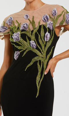 A close-up of the Mac Duggal 11912 Long Beaded-Tulip Formal Dress—a black gown with sheer neckline and intricate purple-green floral embroidery on the chest and shoulders.