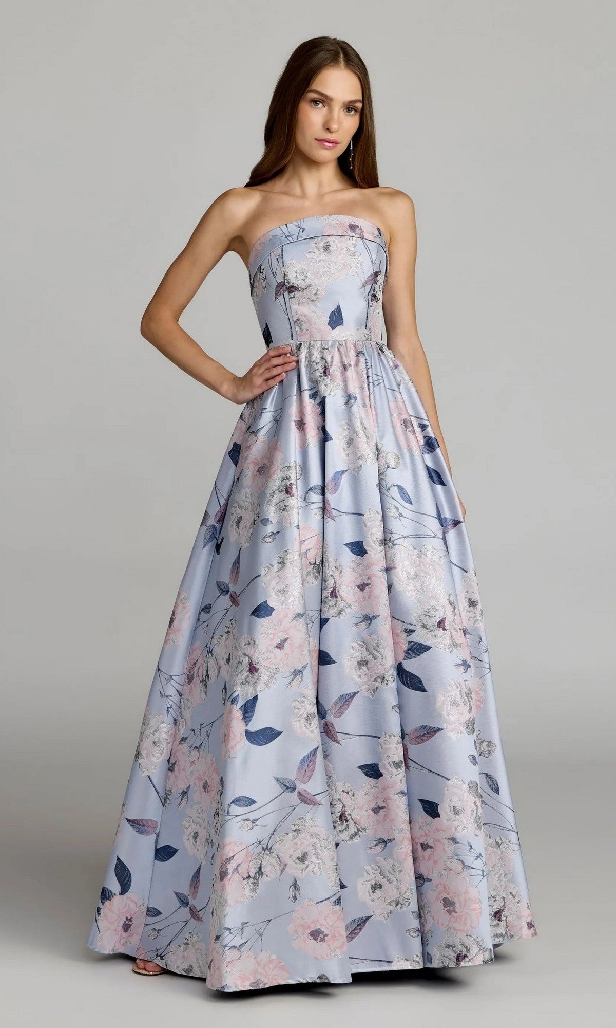 A woman stands wearing the Mac Duggal 11921 long formal dress, a strapless ballgown in a floor-length blue multi floral pattern.