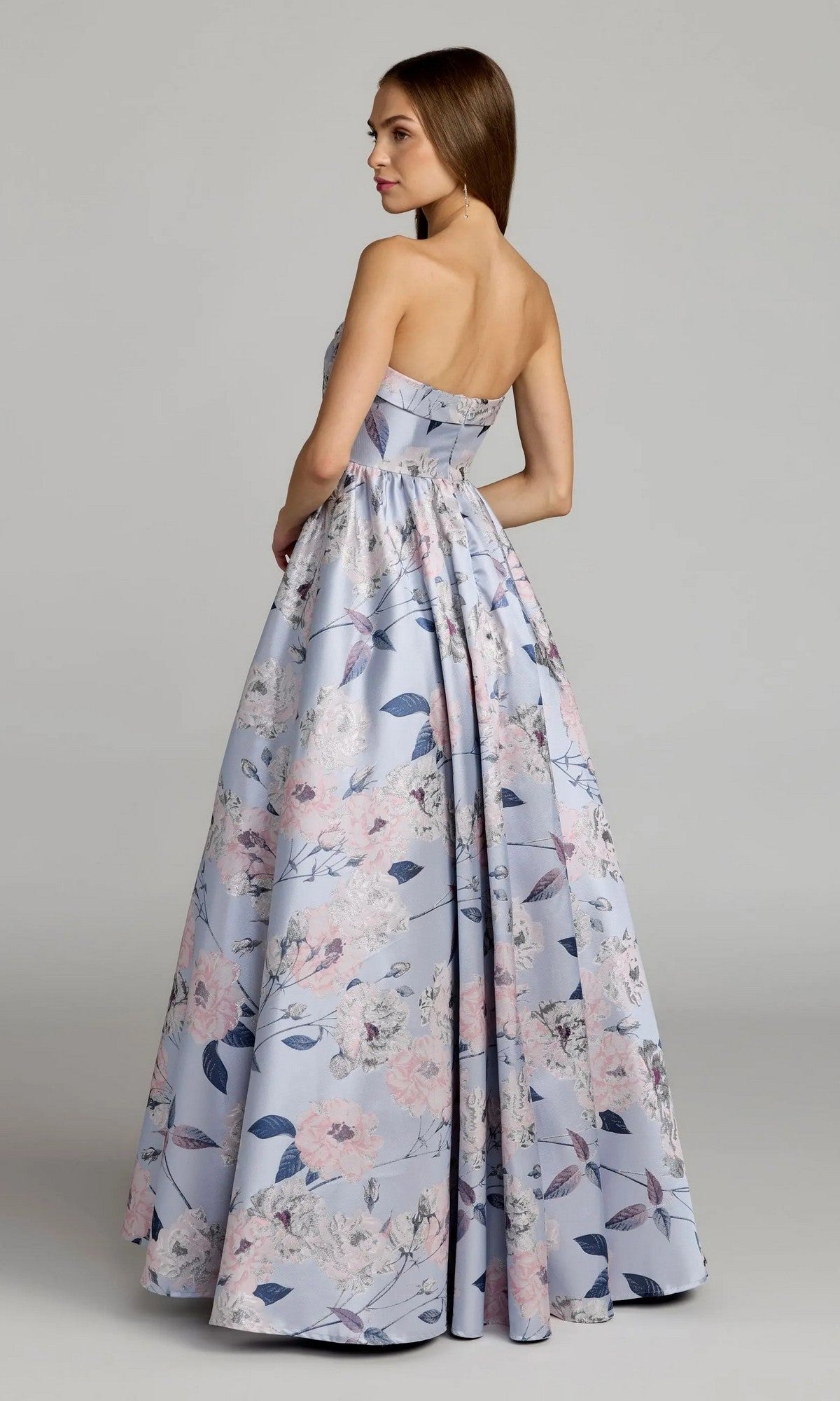 A woman poses in the Mac Duggal 11921 long formal dress—a strapless blue floral ballgown with a light pink and blue pattern—standing slightly to the side against a plain background.