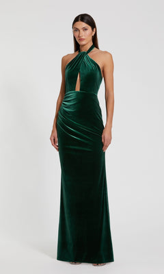 A woman poses in front of a white background wearing the Green Velvet Halter Formal Dress: Mac Duggal 11924, a floor-length emerald gown featuring a sleeveless velvet design and front keyhole cutout.