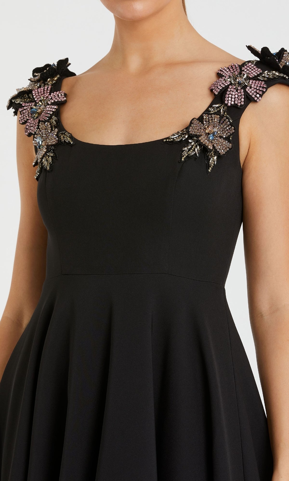 A woman wears the Mac Duggal 11949—a long black A-line formal dress featuring a sleeveless design, square neckline, and embellished floral appliqué on the shoulder straps.