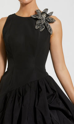 A woman wearing the Mac Duggal 11952 short cocktail party dress, featuring a sleeveless black design with a beaded flower accent on the shoulder and a gathered bubble hem skirt.