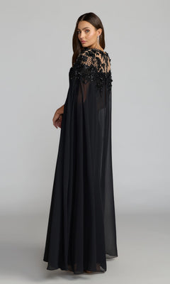 A woman models the Long Formal Dress: Mac Duggal 11954—a black crepe gown featuring chiffon cape sleeves and sequin floral embroidery on the upper bodice—as she stands against a plain studio background.