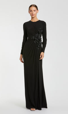 A woman stands wearing the Mac Duggal 11960 long formal dress in black—a modest gown with long sleeves, floral embellishments at the waist, a floor-length skirt, and open-toe heels.