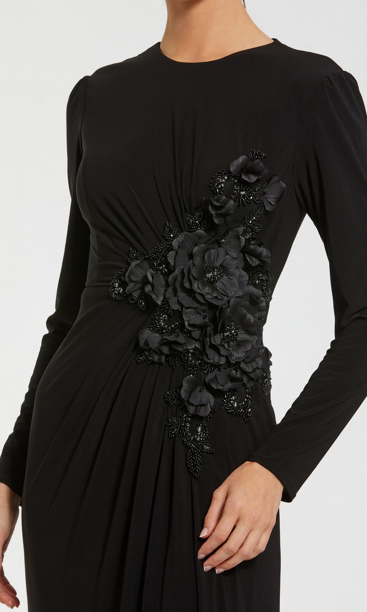 A woman wears the Mac Duggal 11960 long formal dress, featuring long sleeves and black floral appliqué with bead detailing on one side near the waist, for a sophisticated and modest formal look.
