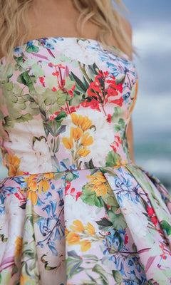 A woman stands outdoors in the Mac Duggal 11991 long formal dress, a strapless floral Mikado gown featuring a high-low bubble hem, with a blurred background.