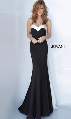 A woman stands against a light background, wearing the Jovani 12020 long formal dress—a black and white strapless satin gown with an elegant mermaid silhouette. The word “JOVANI” appears to the right of her.
