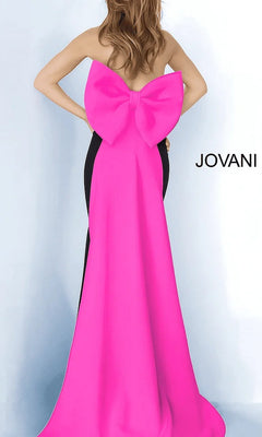 Woman wearing the Jovani 12020 long formal dress in black/fuchsia, featuring a strapless satin mermaid silhouette and an oversized back bow; “JOVANI” logo displayed on the right side.
