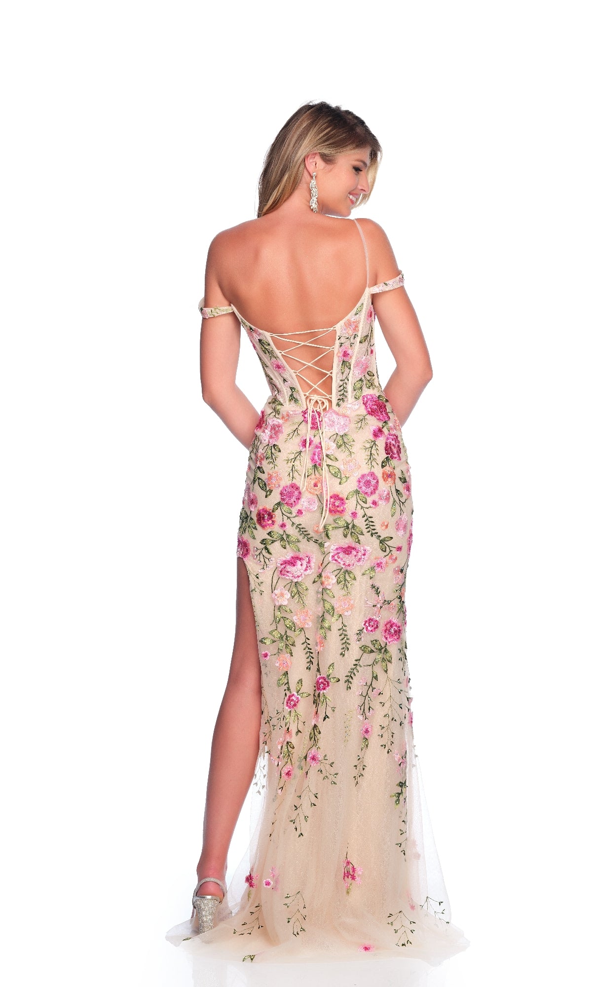 A woman models the Dave & Johnny 12097 long prom dress with an off-the-shoulder lace-up corset bodice and floral embroidery, turned to display the gown’s back against a white background.