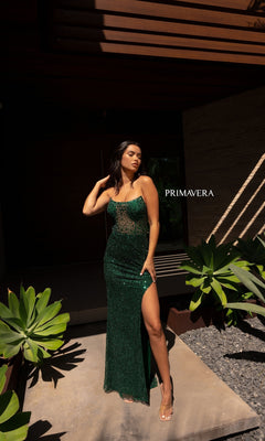 A woman in the Primavera 12123 Strapless Long Beaded Prom Dress with a thigh-high slit stands outdoors by plants, casting a shadow. "PRIMAVERA" is displayed beside her.