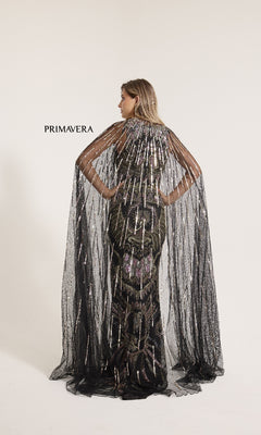 A woman faces away in a sleeveless, black, floor-length Primavera 12177 formal dress adorned with sequins and a sheer sparkling cape, standing before a plain white backdrop. "PRIMAVERA" is displayed on the left.