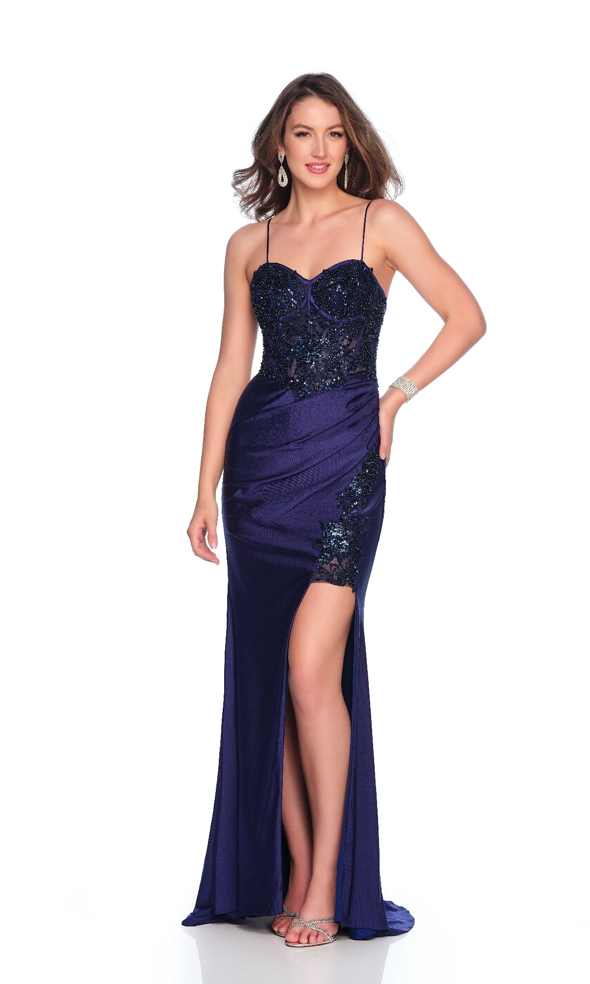 A woman wears the Long Navy Blue Prom Dress: Dave & Johnny 12255, featuring a sequin corset, thin straps, wide leg slit, and silver heels against a white background.