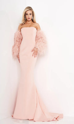A woman stands against a white wall wearing the Jovani 1226 long prom dress in blush pink, featuring dramatic feather sleeves and accessorized with drop earrings.