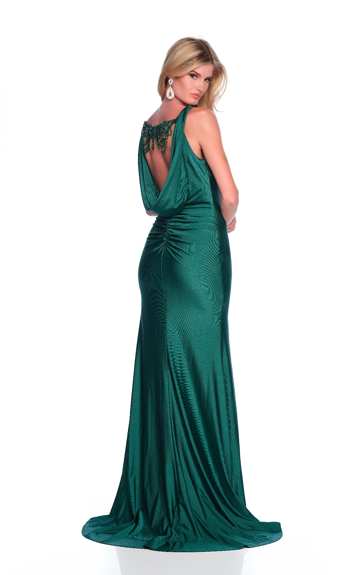 A woman in the Dave & Johnny 12279 long prom dress, featuring emerald green fabric, a draped back, v-neckline, and beaded details, stands facing backward against a white background.