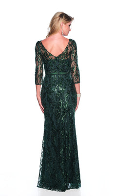 A woman stands facing away, wearing the Dave & Johnny 12317 long sleeve formal dress in dark green with a V-back and sequin embellishments.