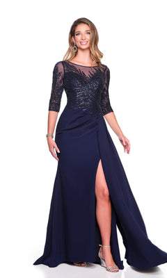 A woman wearing the Dave and Johnny 12363 long formal dress—navy blue with a chiffon embellished bodice, sheer sleeves, and a floor-length sheath skirt with a thigh-high slit—stands smiling against a white background.