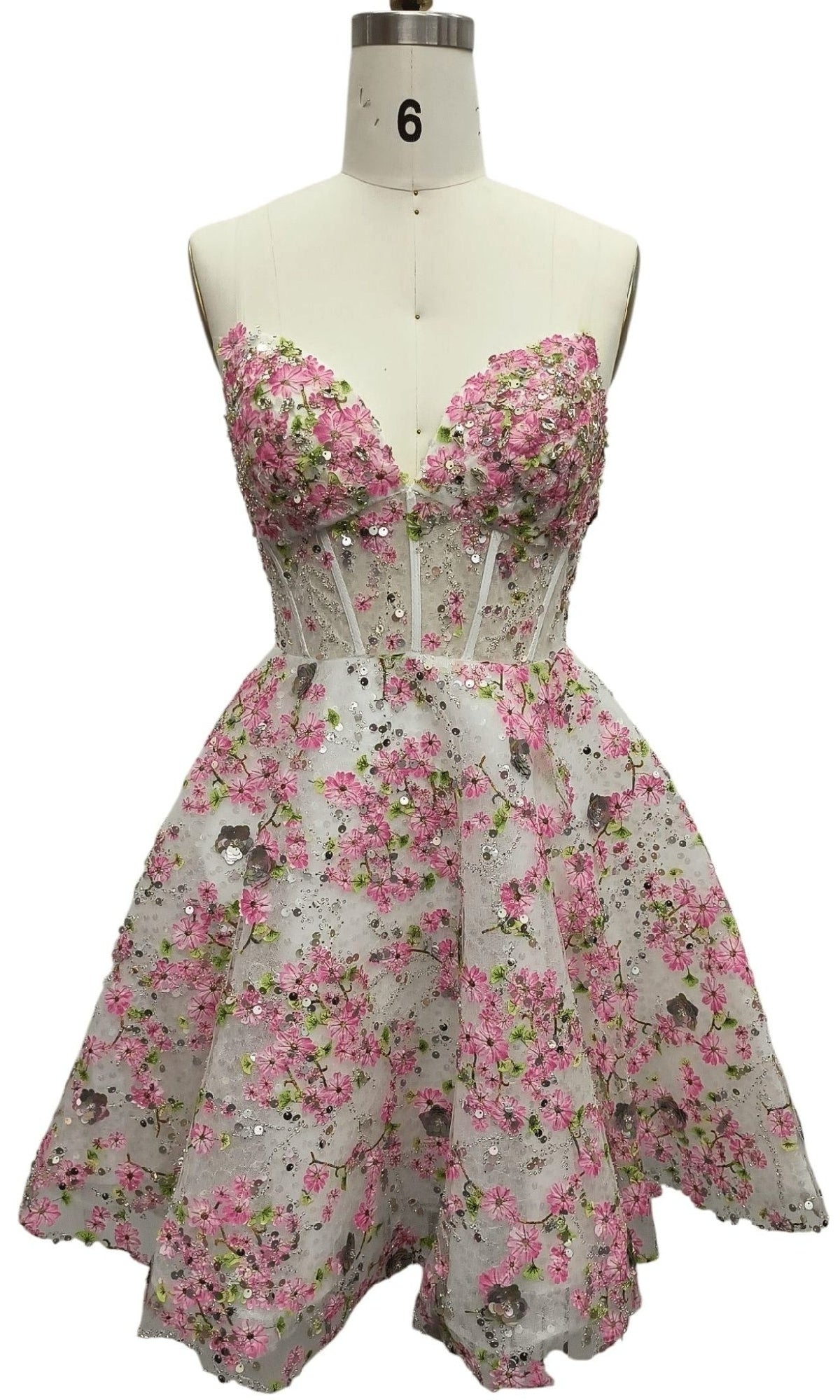 A white mannequin showcases the Strapless Print Hoco Dress: 12375—a short, strapless party dress with pink and green floral designs and a fitted, semi-sheer corset bodice, ideal for homecoming.