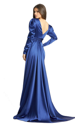 A woman in the Long Formal Dress 12404 by Mac Duggal, featuring long sleeves, royal blue satin fabric, a V-neck, and an open back, stands and looks over her shoulder.