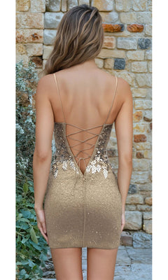 A woman stands outdoors facing a stone wall, wearing Short Homecoming Dress: 12437—a short, backless sequin dress with lace-up back detailing that's perfect for making a statement at your next event.