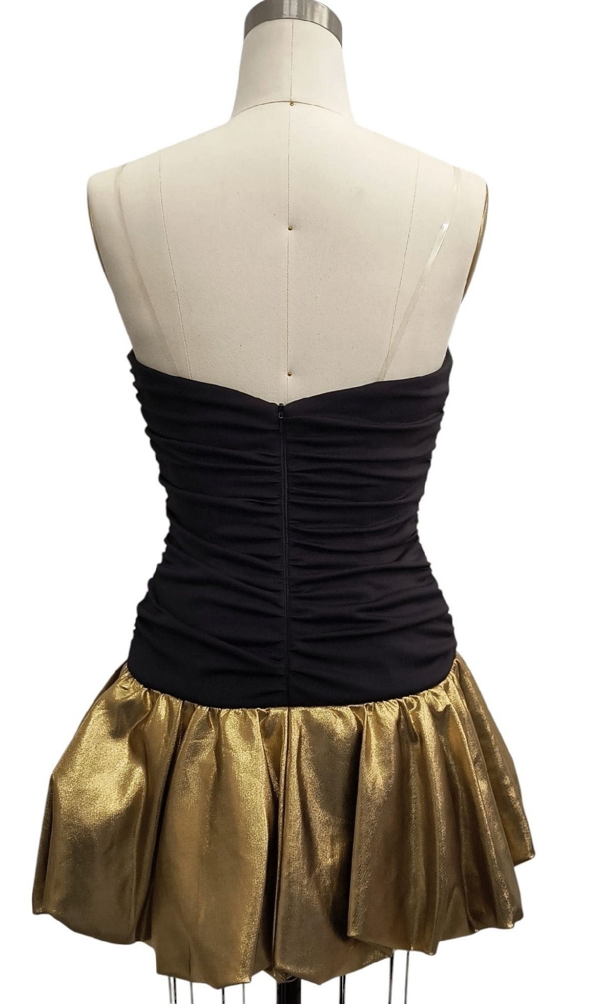 The Strapless Short Hoco Dress: 12483 is displayed on a mannequin, with a ruched black bodice and a metallic gold flared skirt, shown from the back.