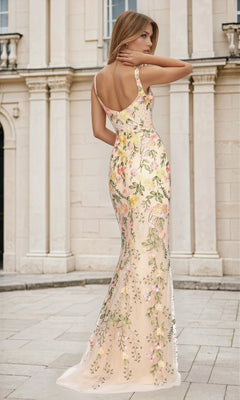 A woman in the Open-Back Floral-Print Nude Long Prom Dress L487 stands outdoors, facing away from the camera before a light-colored stone building.