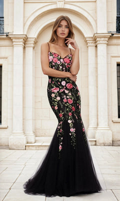 A woman stands outdoors before a stone building, wearing the Floral-Print Black Glitter Mermaid Prom Dress L488 featuring pink floral accents and a flared tulle skirt.
