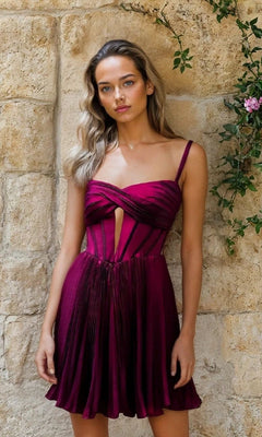 Woman stands against a stone wall, wearing the Fuchsia Pink Short Hoco Dress: 12511, featuring a sleeveless pleated skirt and corset-inspired cut-out bodice.