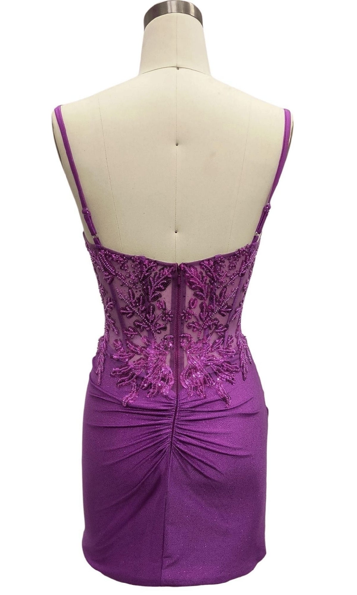 Back view of a mannequin wearing the Bead-Corset Short Hoco Dress: 12515, featuring a purple bodycon fit, thin straps, sheer lace upper back, and lower ruching details for a chic party look.