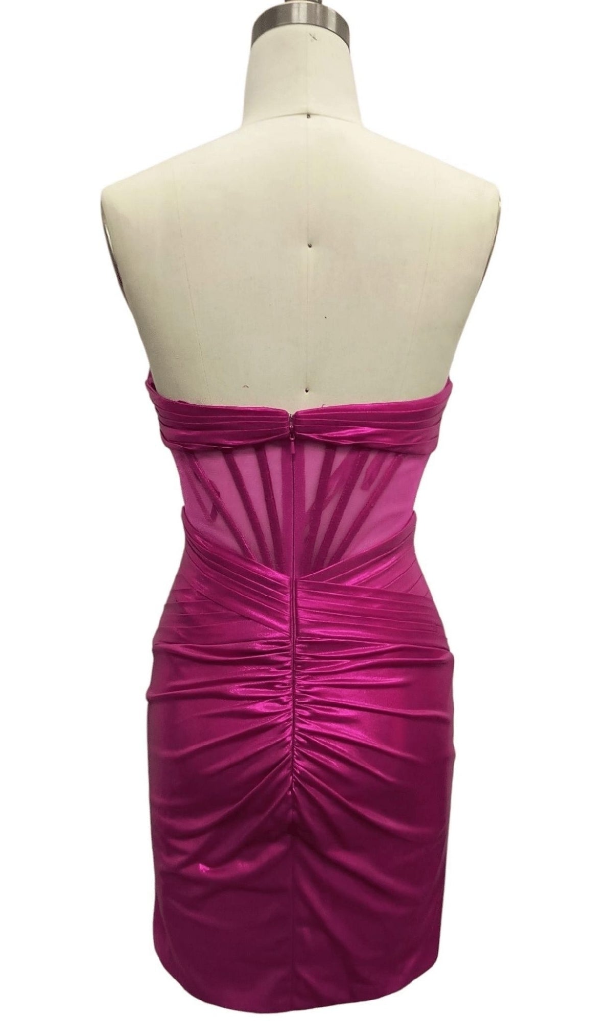 A mannequin showcases the back of the Strapless Fuchsia Pink Hoco Dress: 12565—a fitted, shiny short dress with ruched details, sheer panel accents, and a stylish party-ready look.