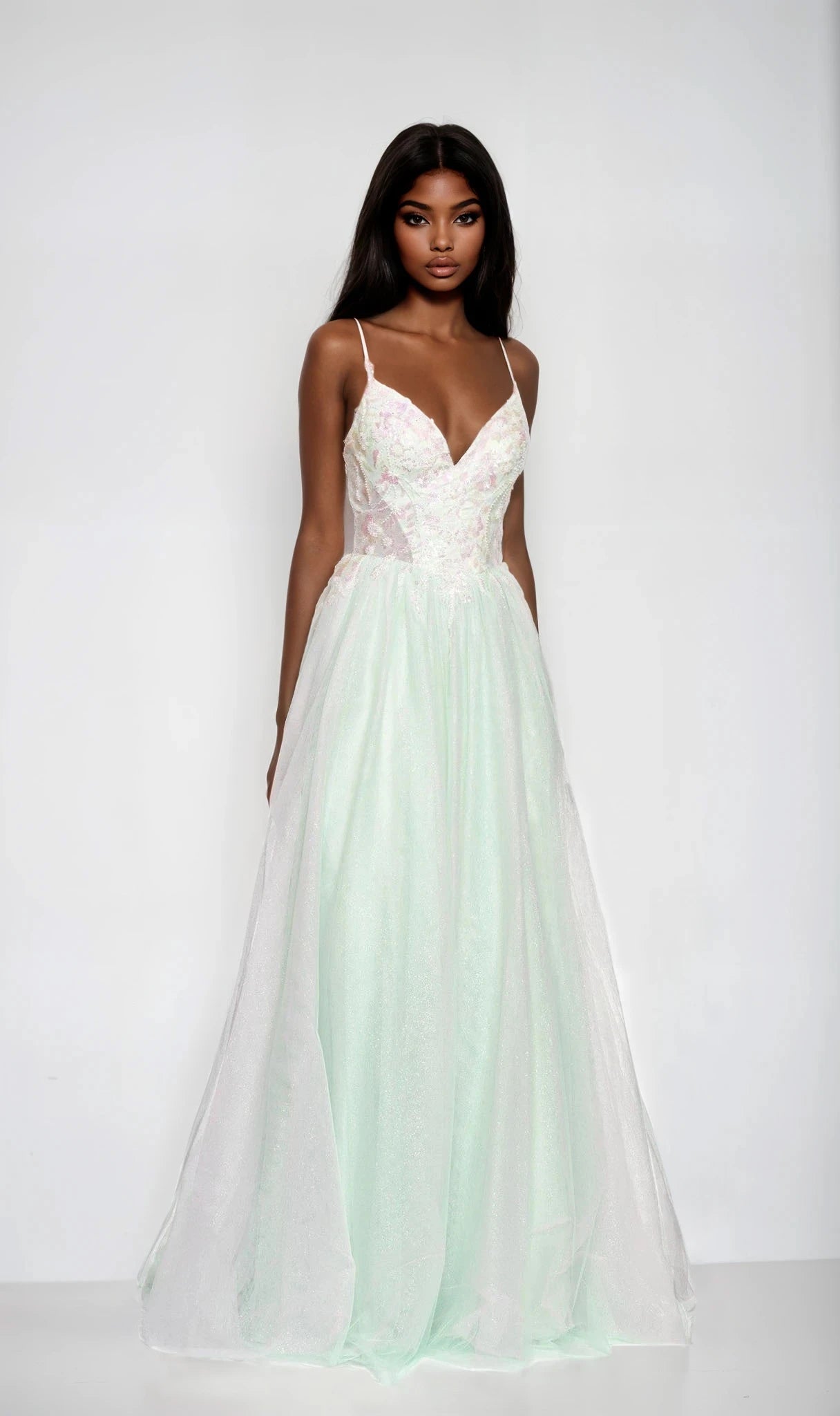 A woman stands against a plain white background wearing the Dave and Johnny 12687 long prom dress, featuring a light green color, embroidered bodice, thin straps, and a flowing tulle A-line skirt.