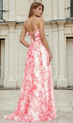 A woman stands outdoors in front of a light-colored building, looking over her shoulder while wearing the Long A-Line Floral Prom Dress L693, which features a pink floral pattern, sweetheart neckline, and lace-up back.