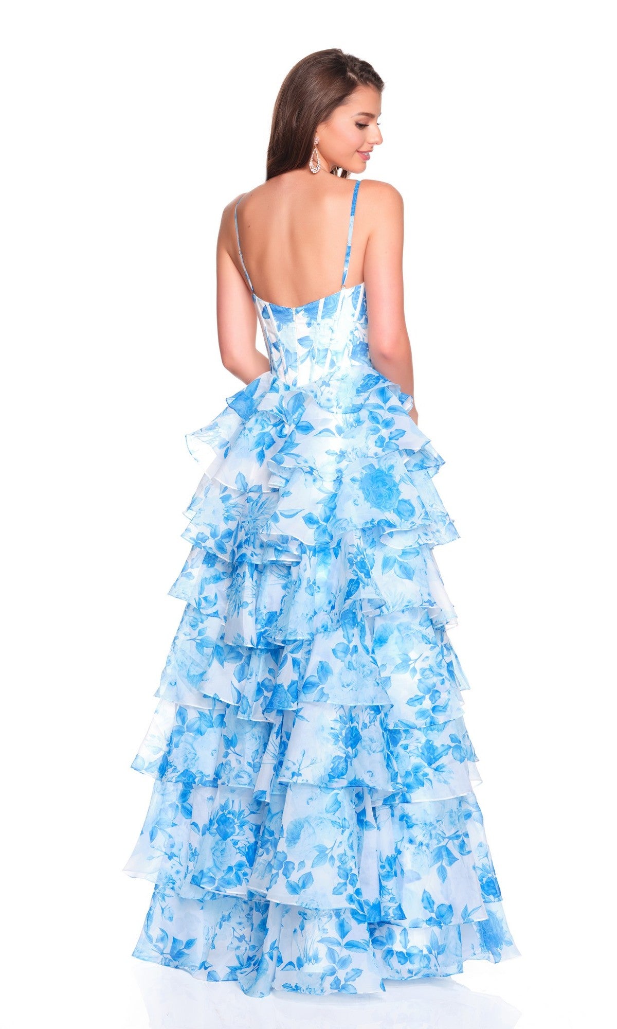 A woman stands facing away, wearing the Dave and Johnny 12809 long prom dress—a sleeveless, backless, floor-length gown with blue and white floral print, corset bodice, and multiple ruffled layers.