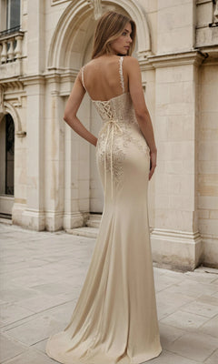 A woman in the Metallic Gold Sheer Corset Long Prom Dress L838, a fitted floor-length gown, stands outside a stone building.