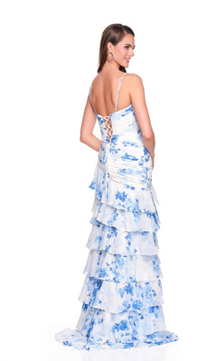 A woman poses with her back to the camera in the Dave and Johnny 12939 long prom dress—a sleeveless, tiered white gown with blue floral patterns and a lace-up open back—set against a white background.