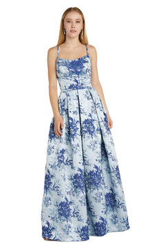 A woman stands against a plain white backdrop wearing the Blue Floral A-Line Prom Dress: Morgan 12945, featuring a sleeveless design, floor-length skirt, elegant A-line silhouette, and cut-out back.