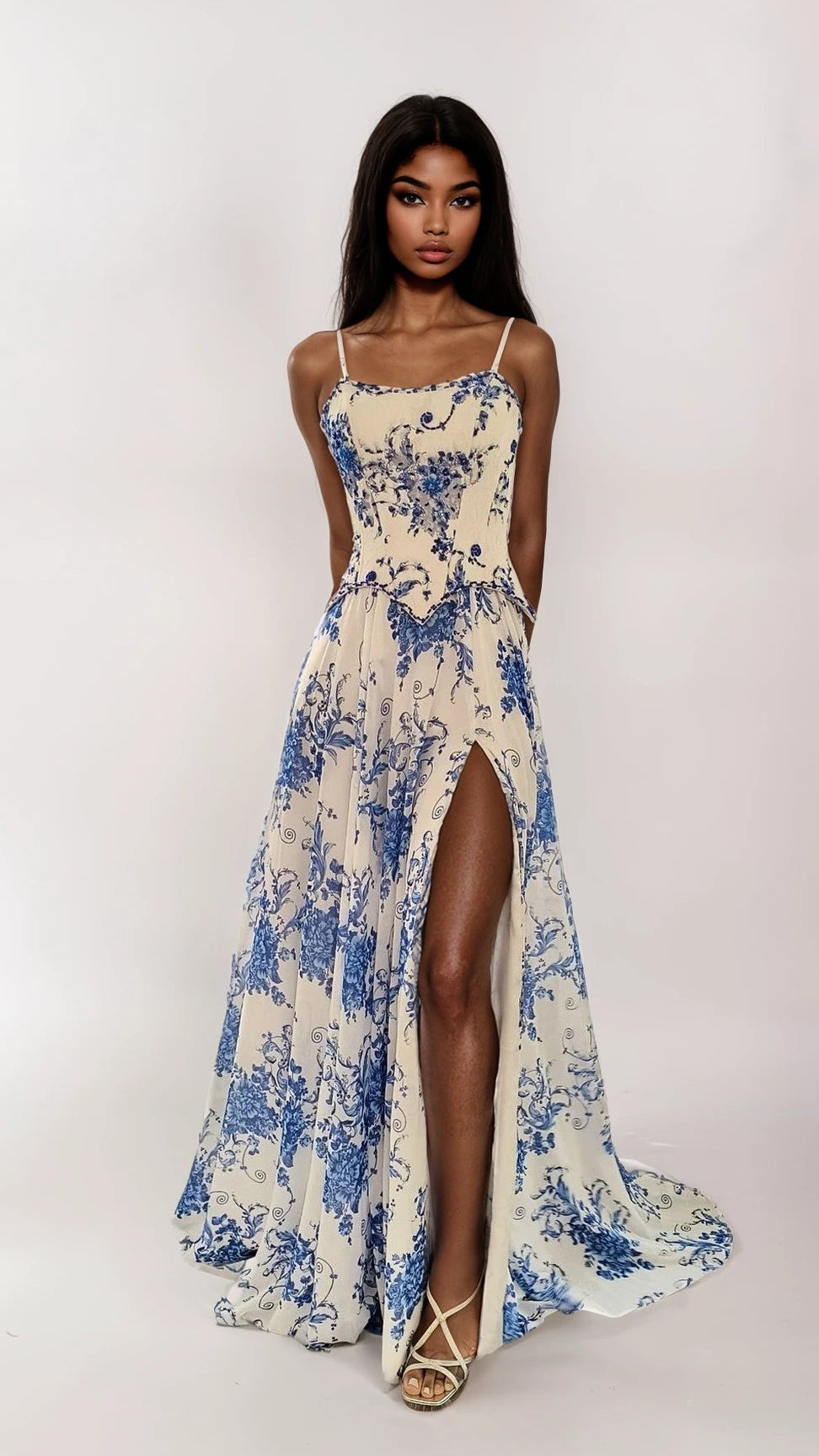 A woman wears the Dave and Johnny 12960 long prom dress, a cream and blue floral gown with a thigh-high slit, paired with strappy heels against a plain white background.