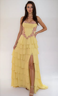 A woman poses against a plain background in the Dave & Johnny 12966 long tiered A-line prom dress in yellow, featuring bead-trimmed corset, pink embroidery, thigh-high slit, and delicate spaghetti straps.