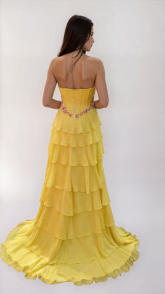 A woman faces away, wearing the Dave & Johnny 12966 long tiered A-line prom dress with a strapless yellow design and floral embroidery at the waist, set against a plain white background.